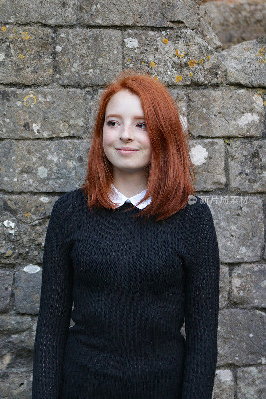 这是一个14 / 15岁的红发少女，皮肤苍白，脸上有雀斑，站在一堵覆盖着青苔的旧石墙前，穿着一件漂亮的休闲装，黑色的，带罗纹的，白色领子的羊毛，造型是一个起伏的短发